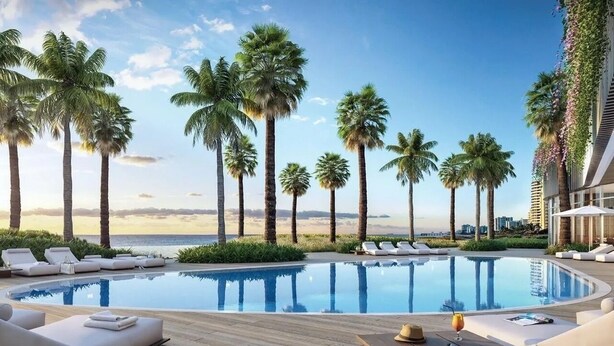 Un espace aménagé au bord de la piscine, avec des chaises longues et une vue sur les palmiers et l’océan.