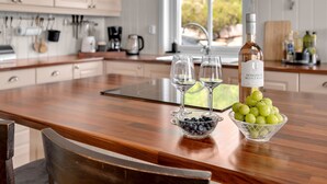 Una cocina con encimera de madera, dos copas de vino, una botella de vino Domaine de Montrose, un cuenco de arándanos y un cuenco de uvas verdes.