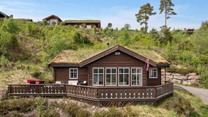 Una cabaña de madera con techo de paja, ventanas amplias y una terraza con mobiliario exterior.