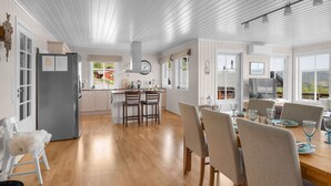 Una cocina amplia con suelo de madera, una zona de comedor con una mesa grande y sillas, y vistas al exterior a través de ventanas amplias.