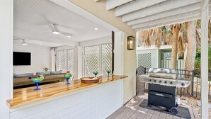 A covered outdoor kitchen area with a grill, a wooden counter, and a seating area with a sofa and decorative items. - 42 Bradley Beach @ Folly Field Beach | Pool | Steps to Sandy Shores | Next to Driessen Beach Park (Hilton Head Island)