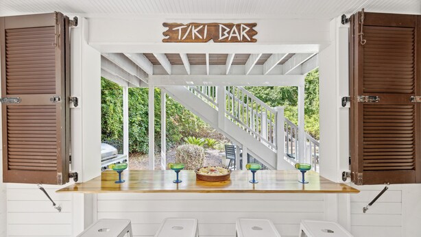 A tiki bar with a wooden sign, white stools, and a view of a staircase leading to a garden. - 42 Bradley Beach @ Folly Field Beach | Pool | Steps to Sandy Shores | Next to Driessen Beach Park (Hilton Head Island)