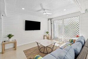 A modern living room with a flat-screen TV, a sofa, a coffee table, and a ceiling fan.