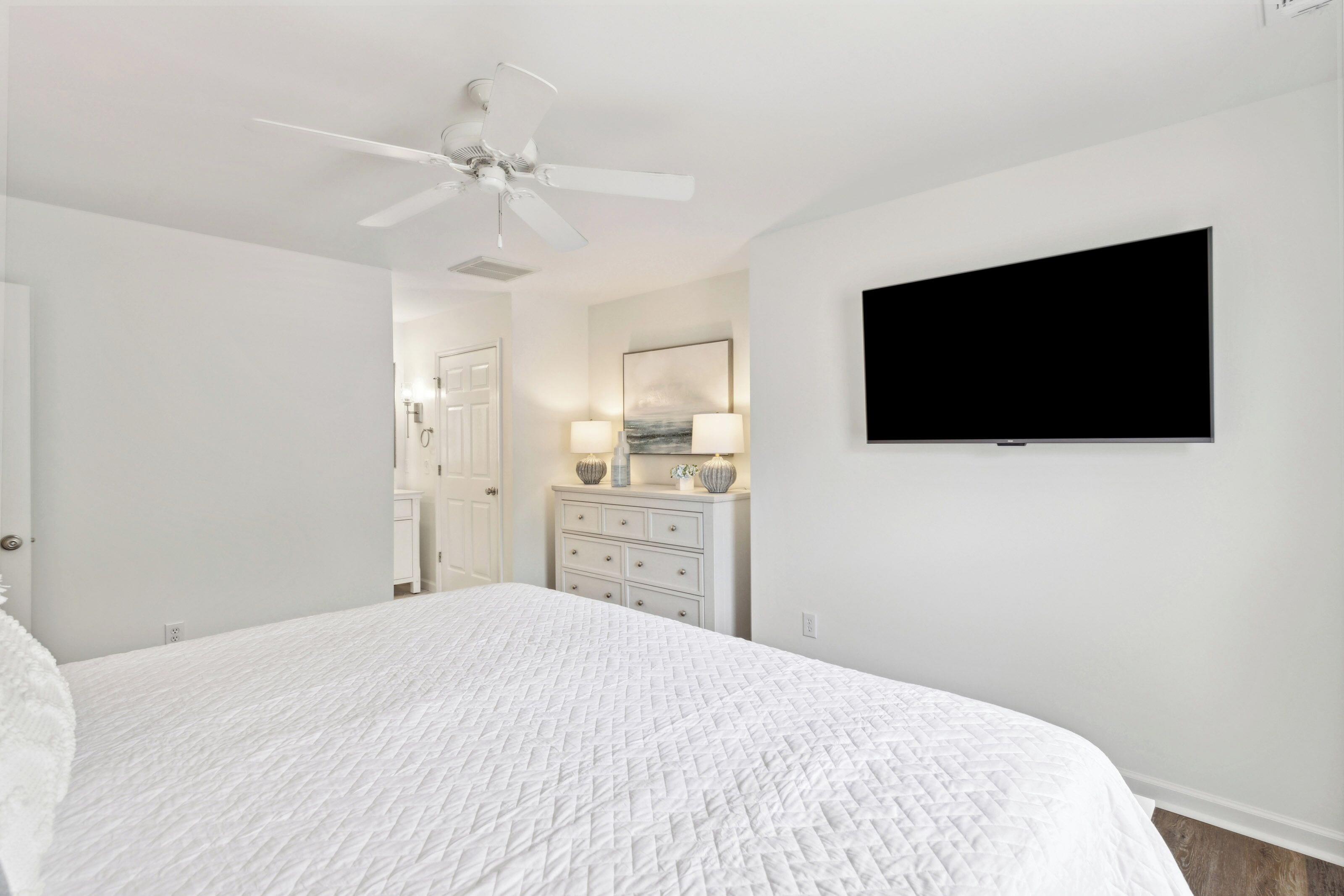 Een slaapkamer met een bed, een plafondventilator, een dressoir, een televisie en een deur.
