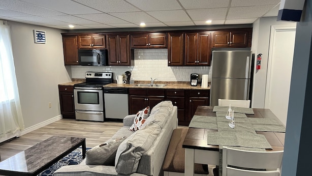 Una cocina compacta con electrodomésticos modernos, un comedor con mesa y sillas, y una zona de estar acogedora con sofá y cojines.