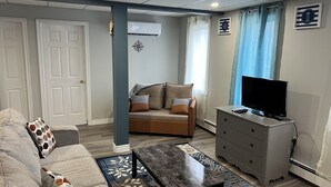 Una sala de estar con sofá, una mesa de centro, un televisor sobre un aparador y un adorno de pared.