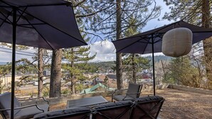 An outdoor seating area with chairs and umbrellas, overlooking a residential area with houses and trees. - Monthly Rental - Crimson 4 BR Cabin By Tahoe Getaways - Walk Downtown Truckee (Truckee)