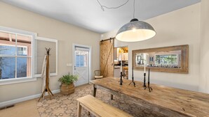 A dining area with a wooden table, bench, pendant light, and a view of the kitchen through a sliding door. - Monthly Rental - Crimson 4 BR Cabin By Tahoe Getaways - Walk Downtown Truckee (Truckee)