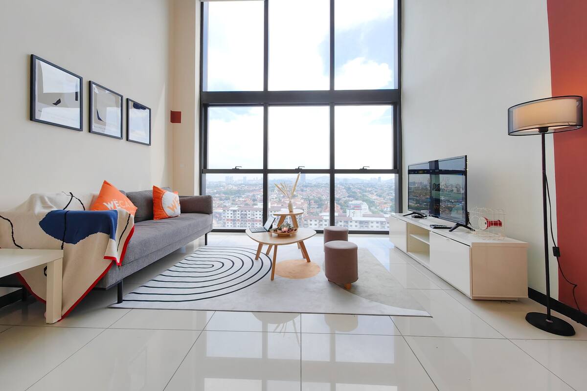 A modern living room with a large window, a sofa with cushions, a coffee table, a TV, and a lamp.