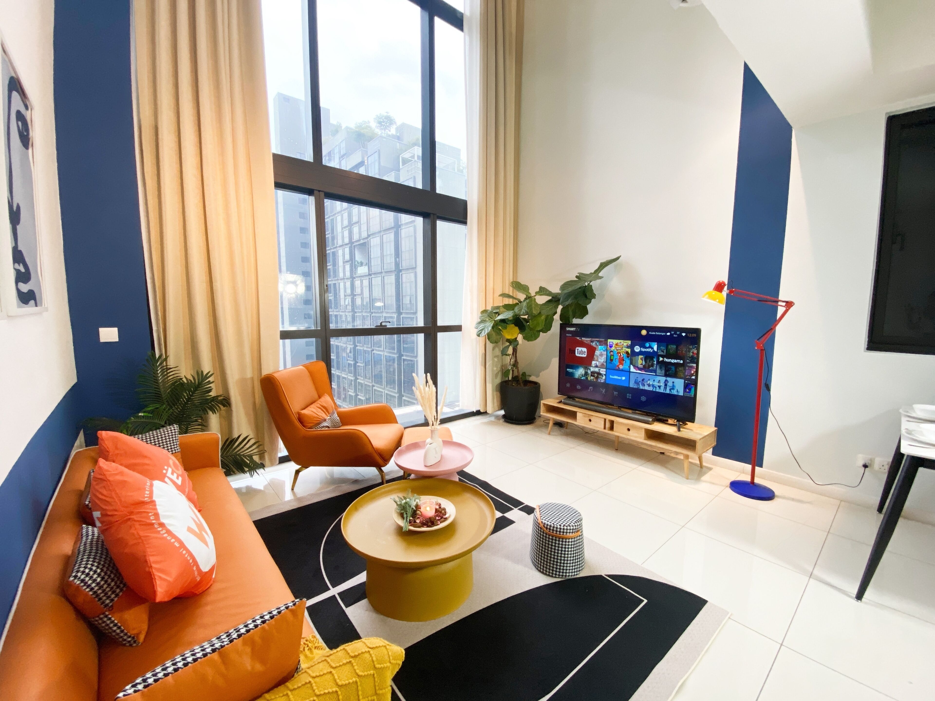 Una sala de estar moderna con un televisor grande, un sofá naranja y una planta en maceta.