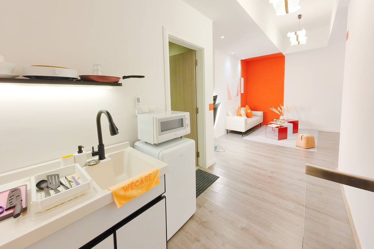 A modern kitchen with a built-in microwave, a sink with a towel, and a dining area with a white sofa and orange accents.