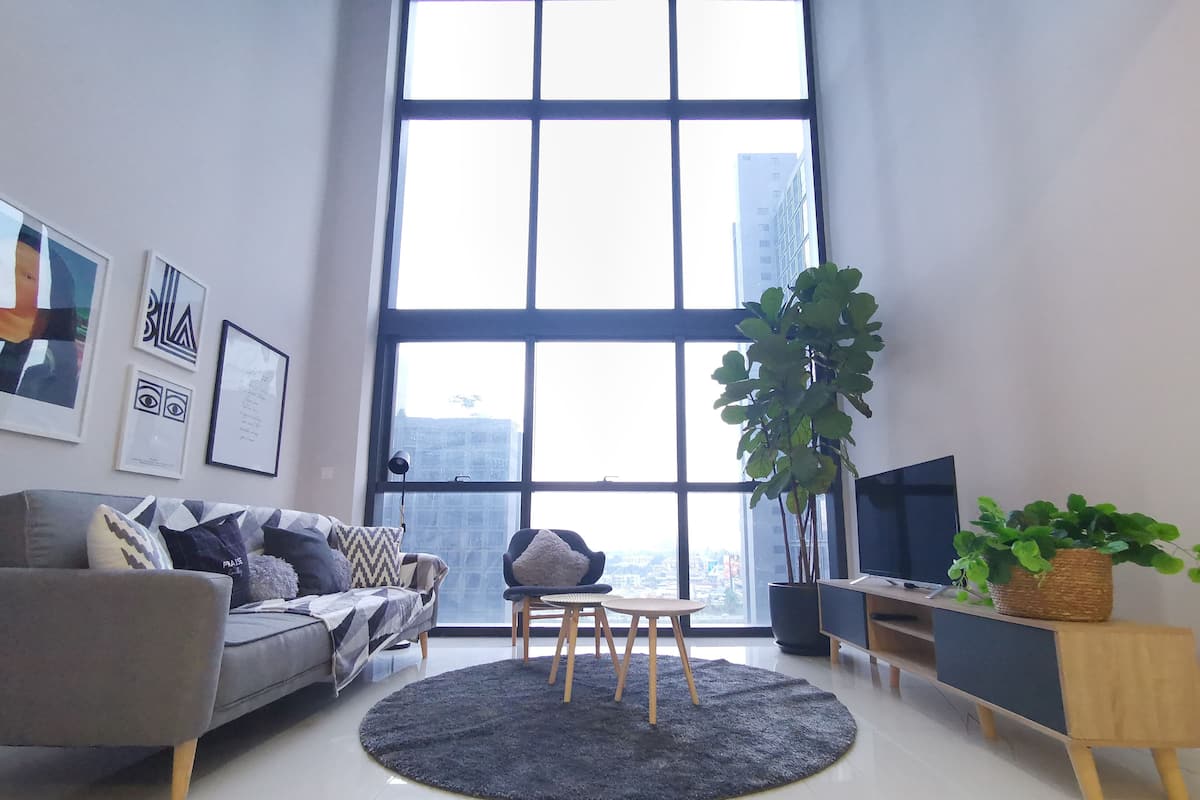 A modern living room with a large window, a grey sofa, a small round table, and a TV.
