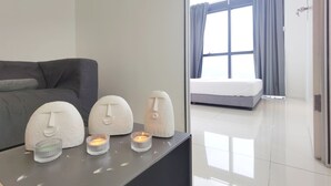 Une chambre moderne avec un canapé gris, une table de chevet agrémentée d’objets décoratifs, un lit avec des rideaux gris et une grande fenêtre.