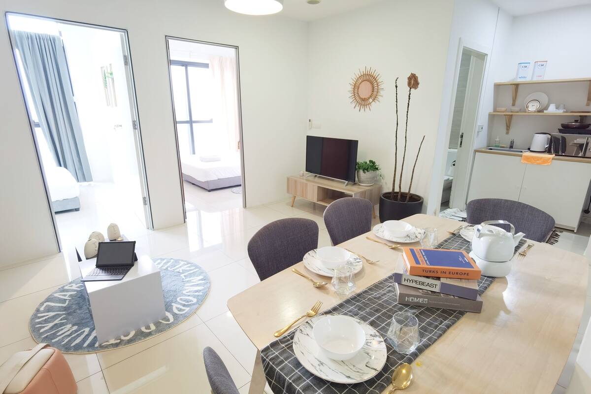 A modern hotel room with a dining area, a TV, a potted plant, and a view of the outside.
