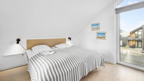 A modern bedroom with a wooden headboard, a large bed with a striped bedspread, two wall-mounted lamps, and two framed pictures.