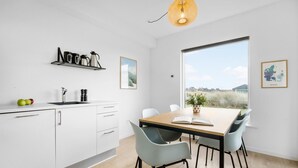 A modern kitchen with white cabinets, a wooden dining table, and a large window offering a view of the outdoors.