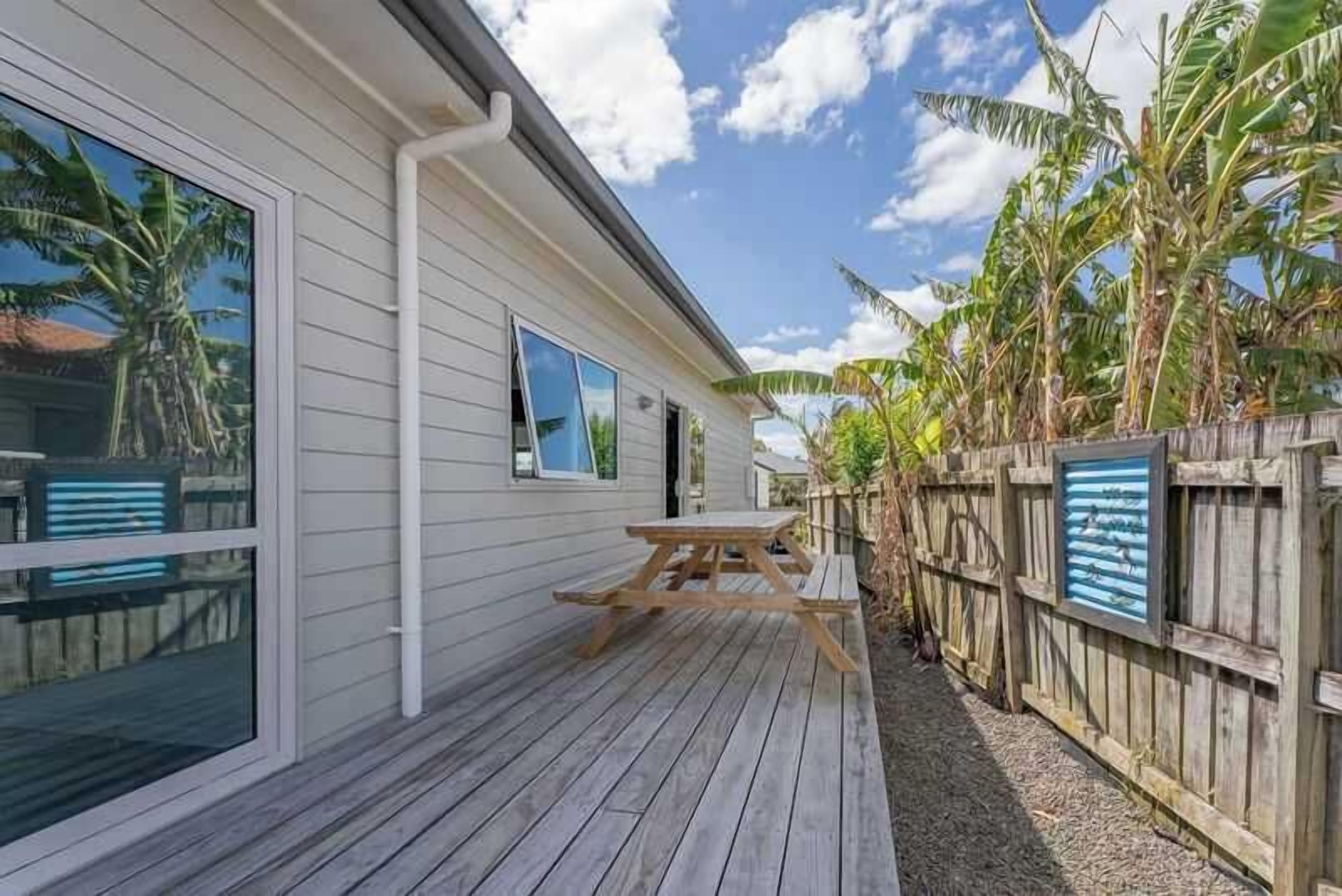 A wooden deck with a picnic table, a white building with large windows, and a wooden fence with a framed picture.