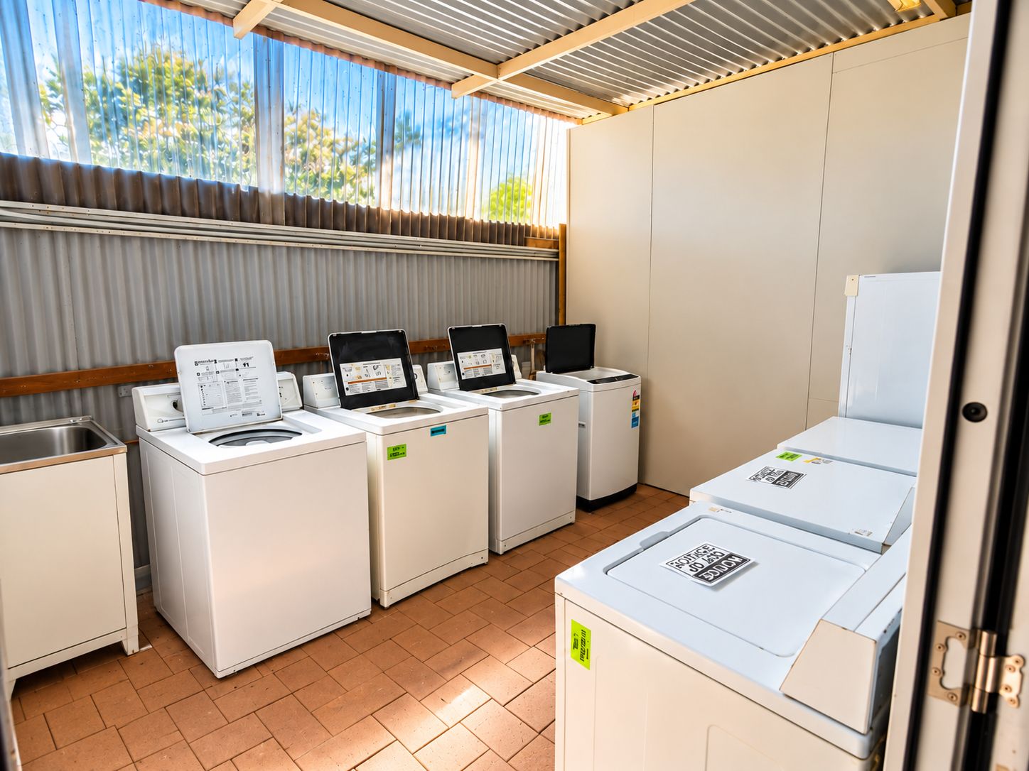 A laundry facility with multiple washing machines and dryers, a sink, and a window with a view of greenery.