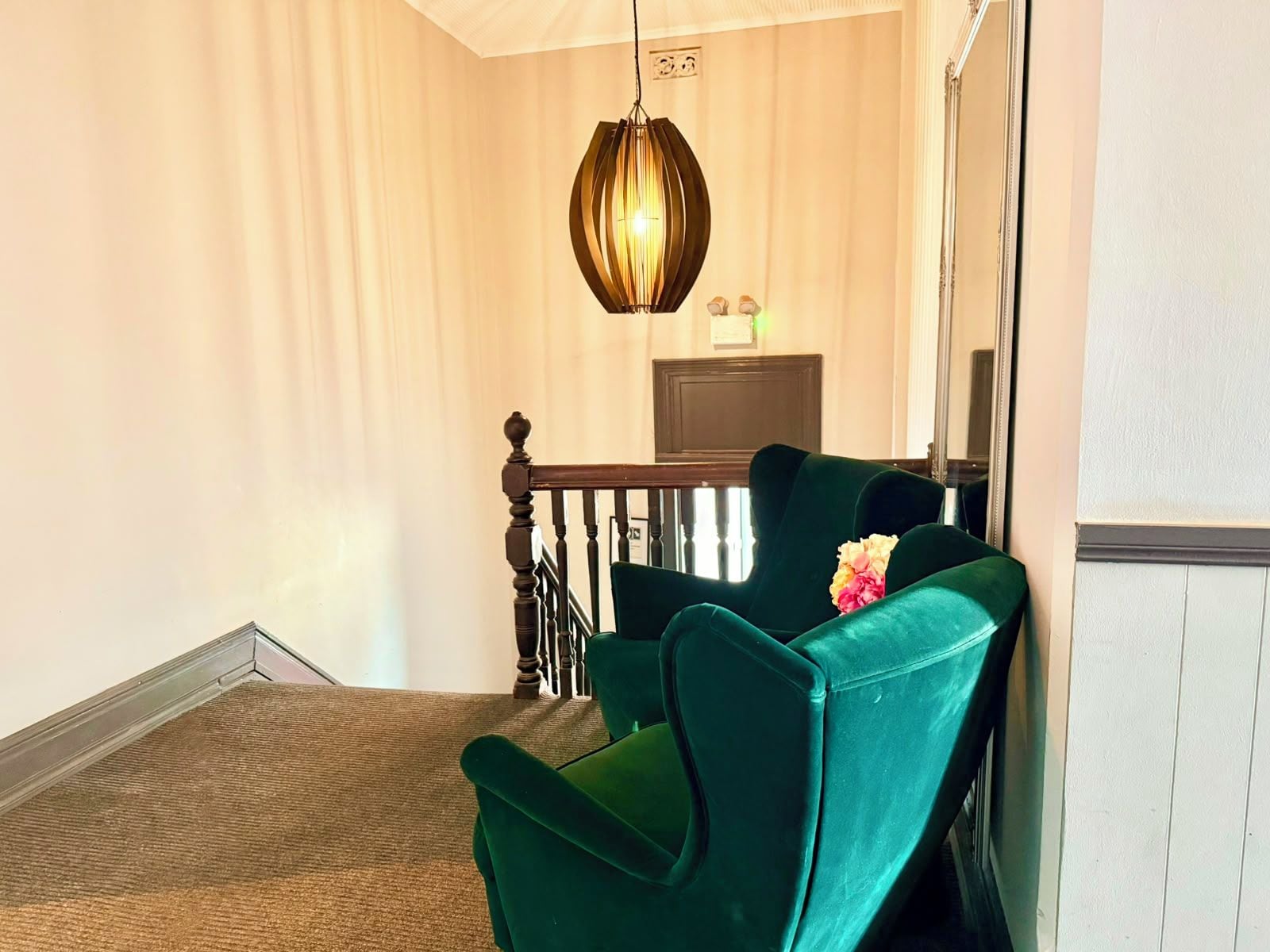 A room with a green chair, a wooden chair, a carpeted floor, a hanging light fixture, and a door.
