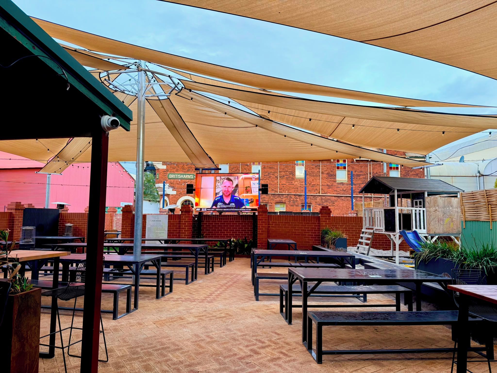 An outdoor patio area with multiple tables and benches, a brick wall, and a large mural on the wall.