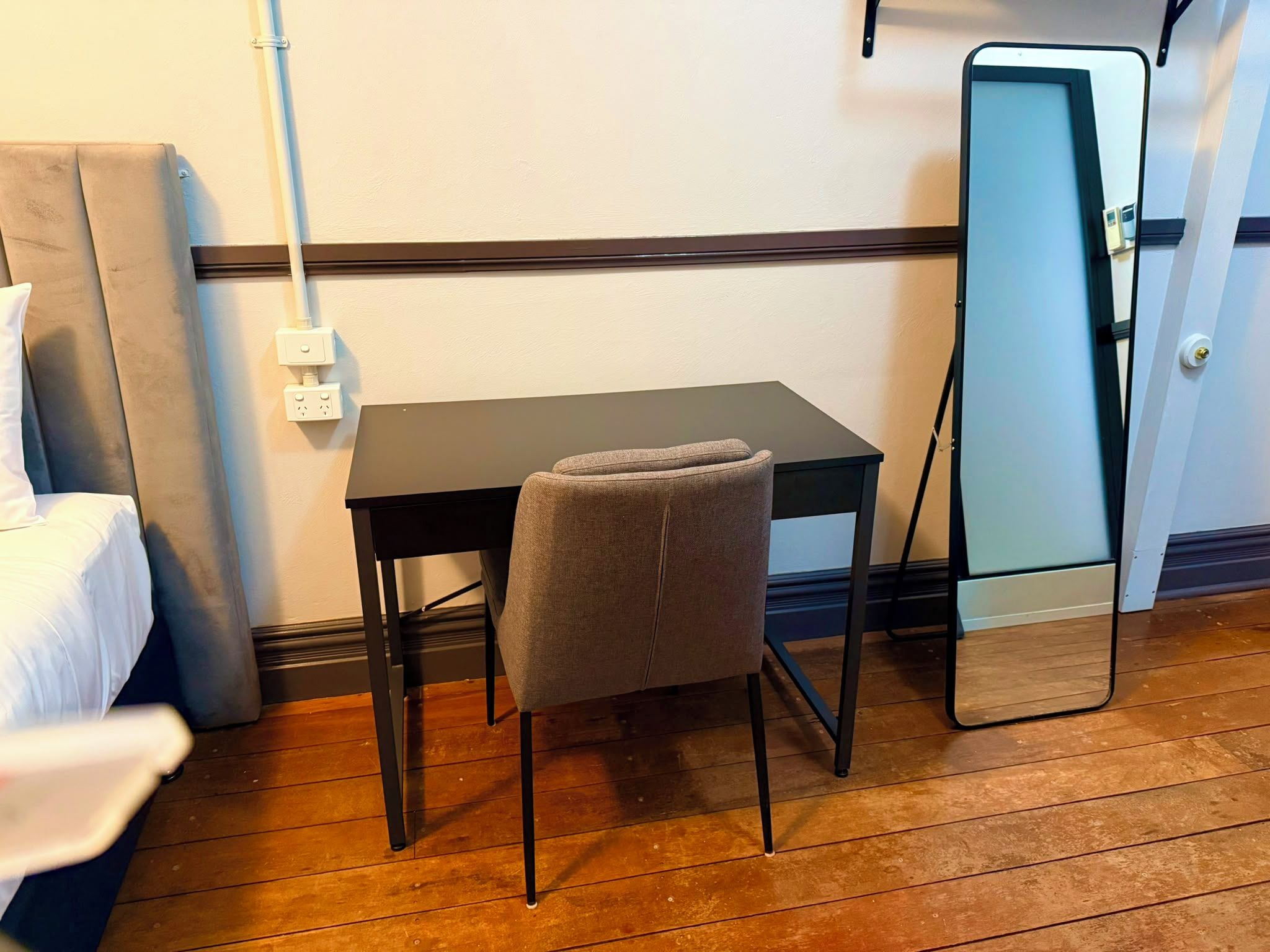 A small room with a single bed, a table, a chair, and a mirror.
