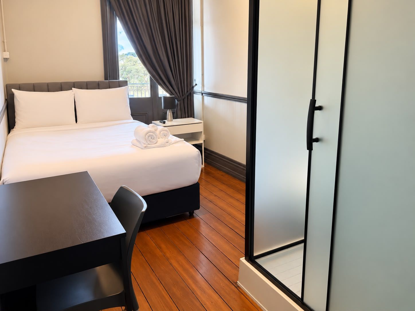 A hotel room with a bed, a desk, a chair, a nightstand, and a wardrobe.