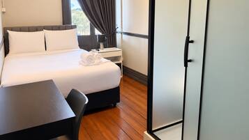 A hotel room with a bed, a desk, a chair, a nightstand, and a wardrobe.