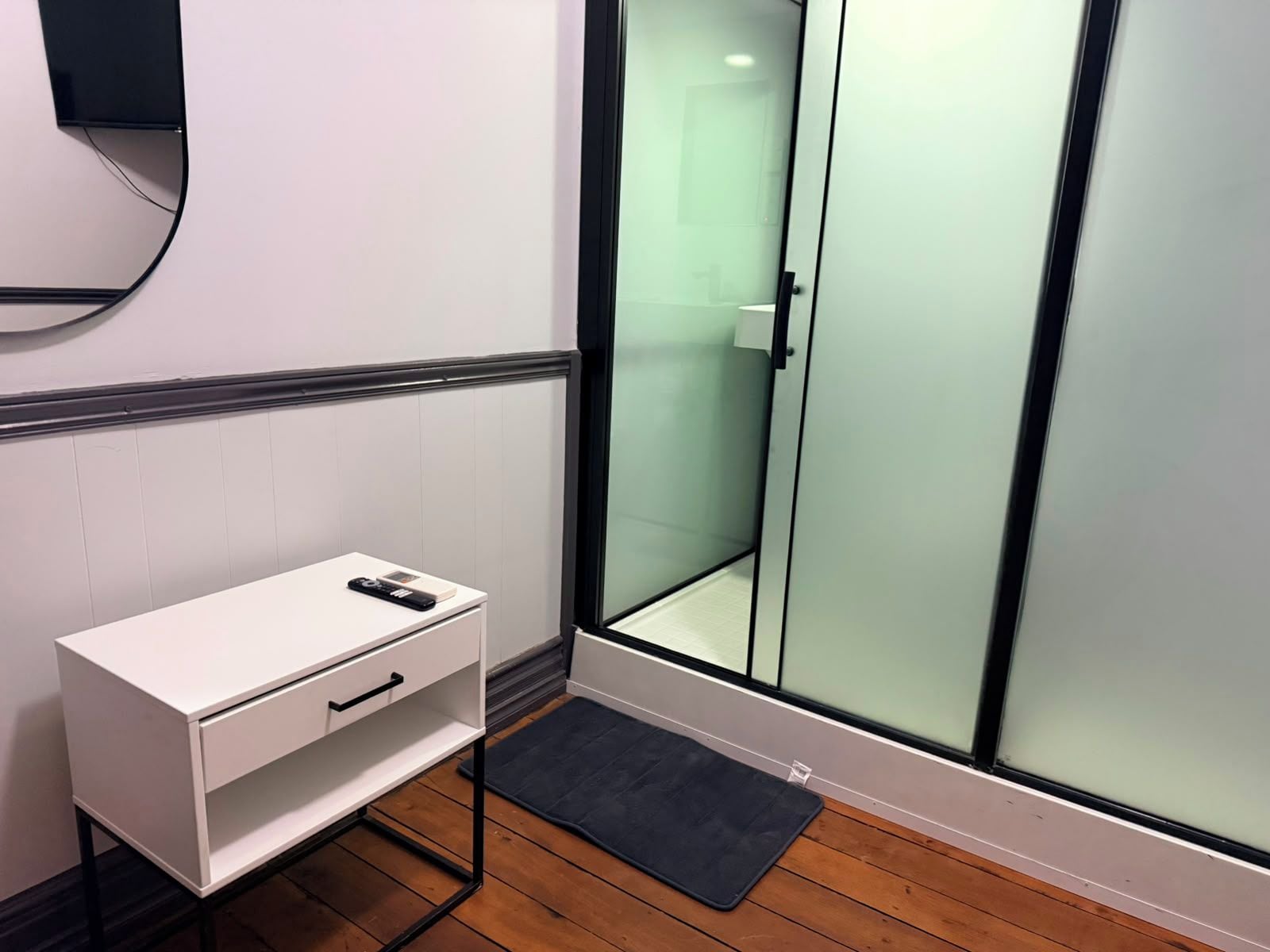 A modern bathroom with a white vanity, a glass shower enclosure, and a wooden floor.