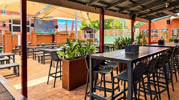 Un patio al aire libre con mesas y sillas, un muro de ladrillo y una pantalla de televisión.