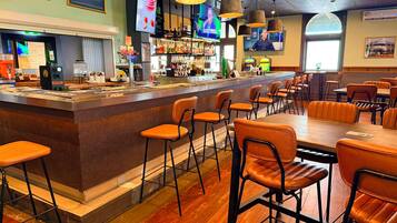A bar area with stools, a counter, and a television screen.