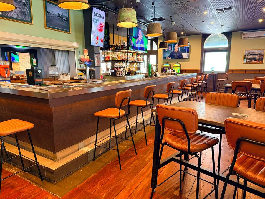 Zona de bar con taburetes, barra y una pantalla de televisión.