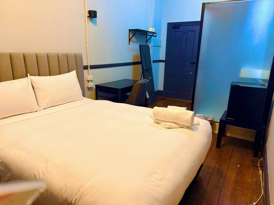A hotel room with a large bed, a desk, a chair, a wardrobe, and a mirror.