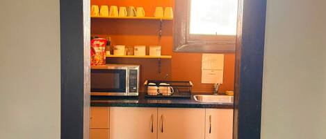 Una cocina con microondas, hervidor y tetera en la encimera.