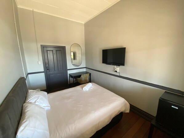 Una habitación de hotel con cama, escritorio, silla, televisor y puerta.