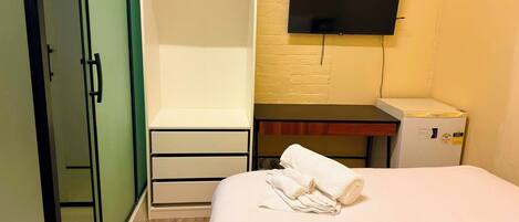 A hotel room with a bed, a wardrobe, a desk with a flat-screen TV, and a small refrigerator.
