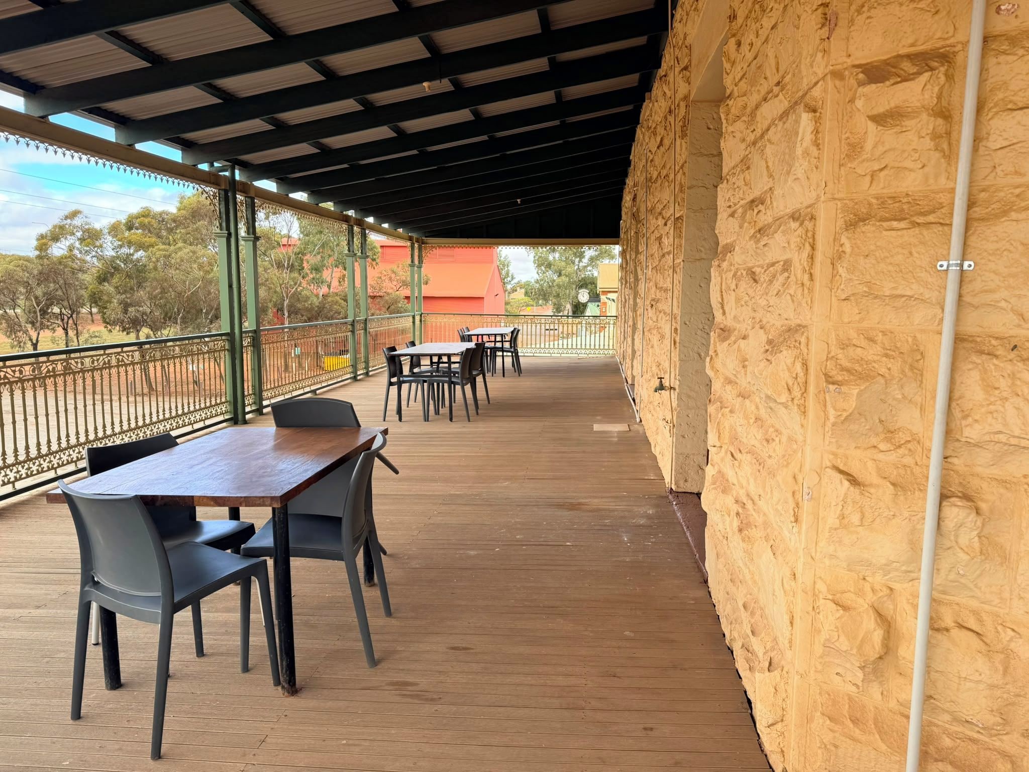 An outdoor patio with tables and chairs, a stone wall, and a metal railing.