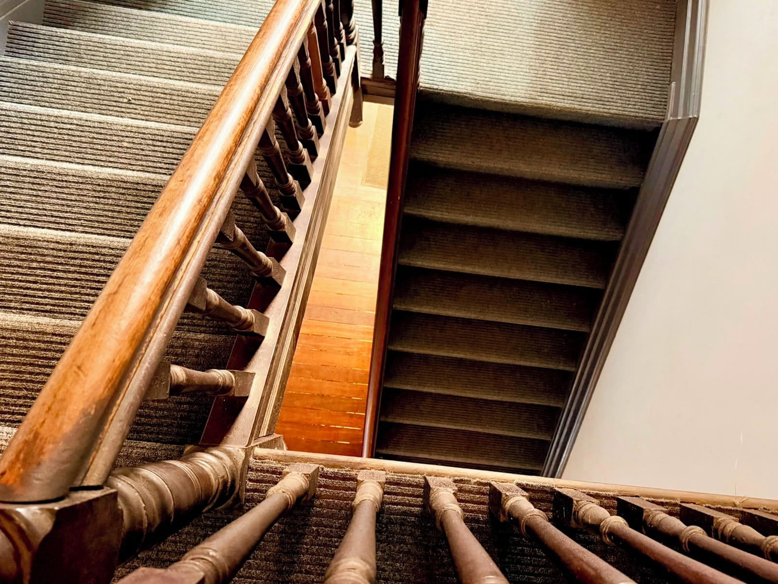 A wooden staircase with a handrail and carpeted steps leading to a landing.