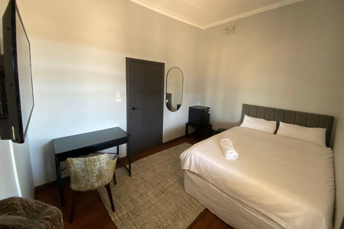 A hotel room with a bed, a desk, a chair, a mirror, and a television.