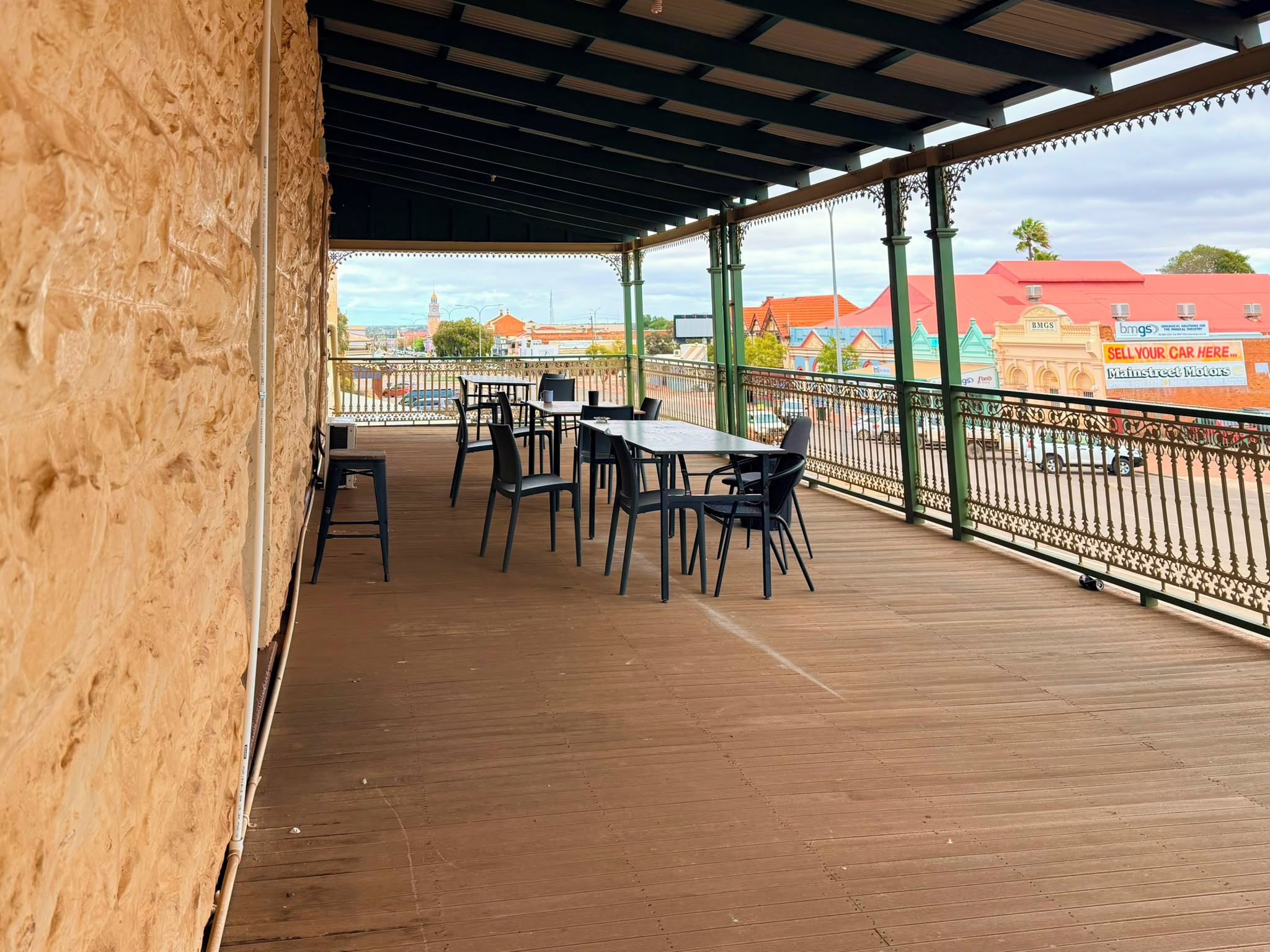 An outdoor patio with tables and chairs, a wooden floor, and a view of buildings in the background.