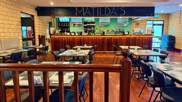 A restaurant interior with multiple tables and chairs, a bar area, and a sign reading 'MATILDA'S DRINKS'.