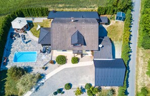 En vy från ovan av ett hus med en stor huvudbyggnad, en swimmingpool och ett garage.