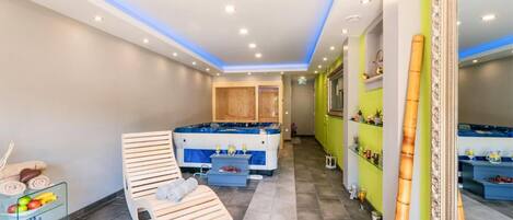 A modern spa room with a wooden massage table, a hot tub, and a mirror.