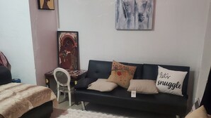 A cozy living room with a black sofa, a red ottoman, and a white shag rug. There are two framed artworks on the wall and a small side table with a chair. - 420 Friendly South Beach Miami  (Miami Beach)