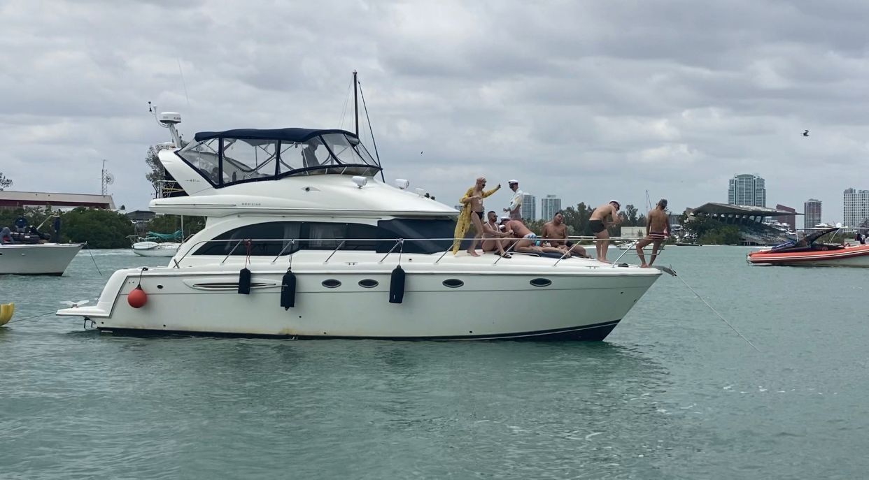 Un yacht avec plusieurs personnes sur le pont, une vue sur les gratte-ciel d’une ville en arrière-plan et une eau calme.