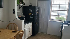 A compact kitchen with a dining area, white cabinets, a black refrigerator, and a window with blinds. - 420 Friendly South Beach Miami  (Miami Beach)