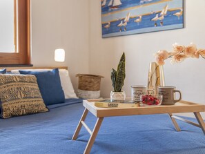 Una camera da letto accogliente con un letto, cuscini, un vassoio con libri e una pianta, e un quadro appeso al muro.