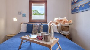 Un dormitorio con cama, una mesa de madera con una bandeja, un florero con flores y un cuadro en la pared.