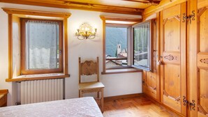 Une pièce aux murs en bois, avec un lit, une chaise et deux fenêtres équipées de rideaux.