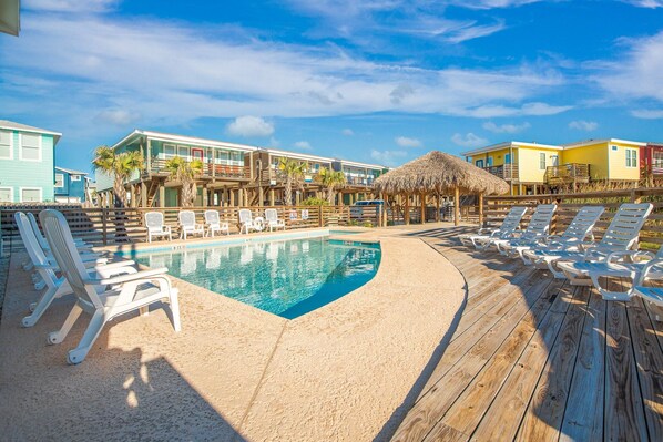 A pool area with lounge chairs and a wooden deck. - Sandy Coral | Community Pool + Pets | Near Beach (Port Aransas)