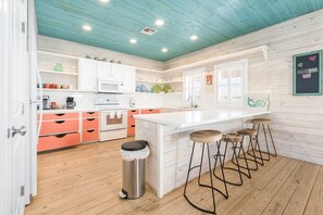 Une cuisine moderne avec des meubles blancs, un îlot central doté de tabourets et un plafond en bois.